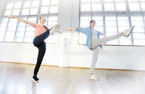 Two girls with outstretched arms standing on one leg while stretching forwards the other one during training class