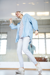 Young female dancer in activewear listening to energetic music in headphones and moving by the sounds