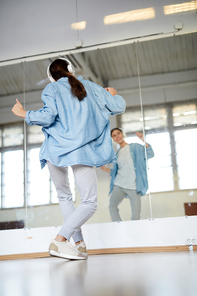 Back view of young dancer with headphones training in front of large mirror in studio