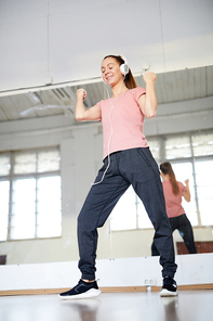 Young active energetic dancer with headphones moving by music sounds while training in studio