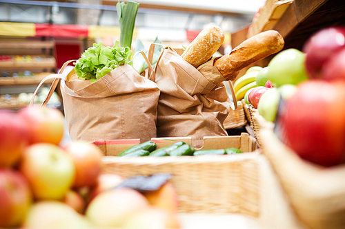 Close-up of shopping bags full of fresh products such like bread vegetables and greens on counter