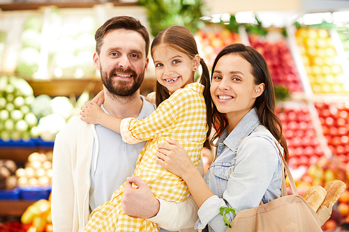Cheerful friendly young family embracing and standing organic food store while 