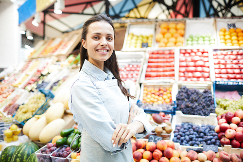 Smiling confident brunette female grocery retailer working at farmers market and selling fresh healthy fruits and vegetables, she 