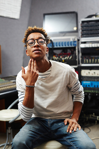 Young cool guy in casualwear and eyeglasses making gesture with his fingertips behind chin