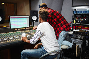 Guy with drink and sound operator looking at monitor while adjusting sounds on switchboard