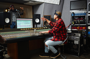 Soung operator sitting by switchboard in front of monitor and talking to musician while recording songs