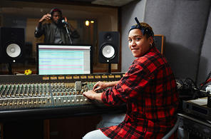 Young professional sound operator sitting by soundboard and recording voice of singer