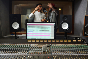 Soundboard with faders and mixers and computer monitor with two men singing on background