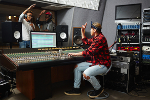 Sound operator showing okay gesture to young musicians while recording their songs in audio studio