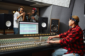 Two young singers performing their songs in record studio with help of operator