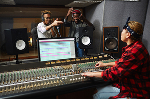 Excited musicians performing their songs in studio in front of operator making records