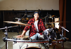 Young contemporary drummer sitting in studio or garage in front of drum set