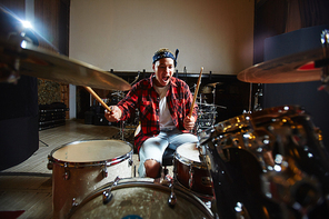 Emotional rock band performers practicing drum play in garage