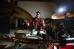 Young African-american woman with drumsticks playing in audio studio