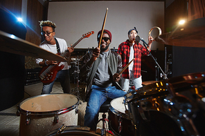 Band of young drummer, guitarist and singer playing instruments and performing songs in studio of records