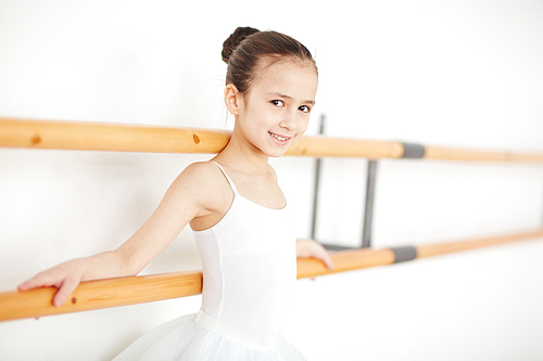 Little ballerina with strict hairstyle staying in light dancing studio and 