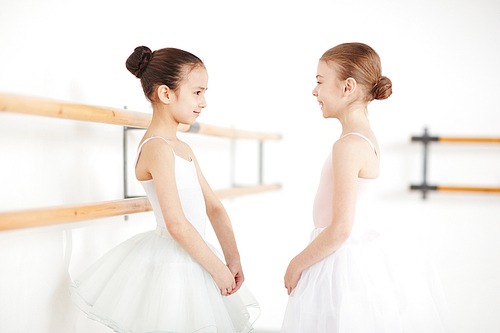 Young ballerinas with strict hairstyle staying and smiling in white room with sunlight