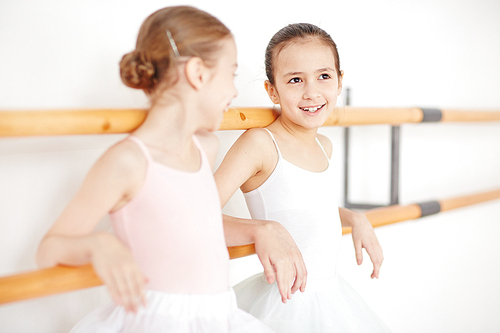 Young ballerinas in white clothes smiling and talking in dancing school with sunlight