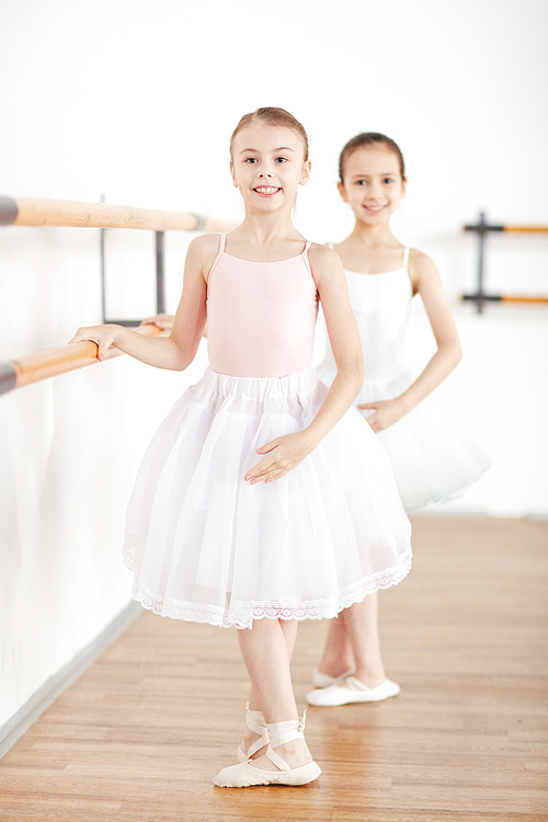 Little girls in white tutu and light pointe making position in dancing school