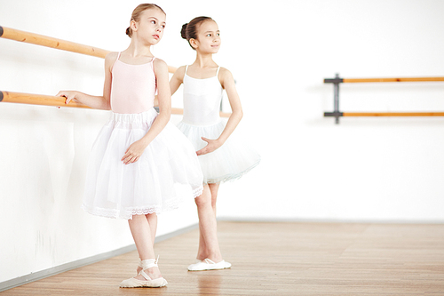 Little ballerinas making position in white clothes at wooden machine in school