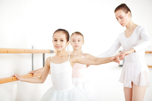 Little girls practicing dances at wooden machine with pedagogue in white class