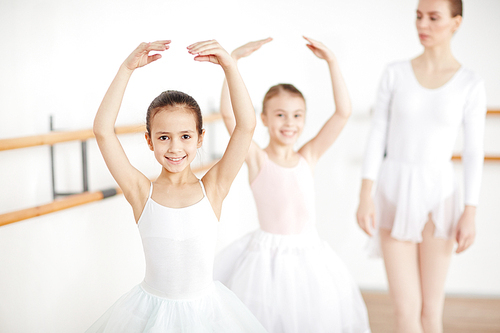 Pretty young ballerinas smiling and staying in pose in white room with adult teacher