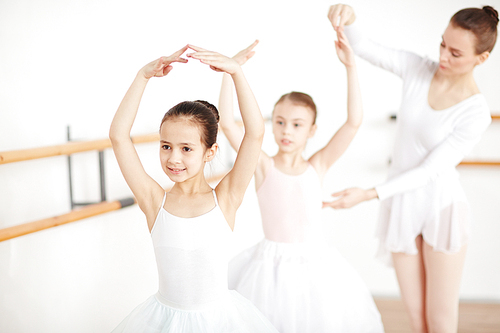 Little ballerina dancing with her arms over head while teacher helping her friend near by