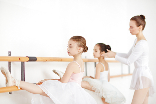 Young girls in ballet dresses keeping their left feet on bars while making stretch