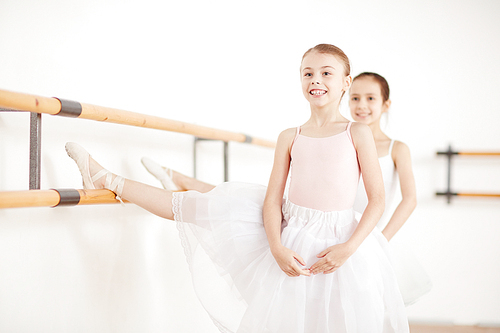 Pretty girls in tutu and pointe doing stretching in light dancing studio and looking away