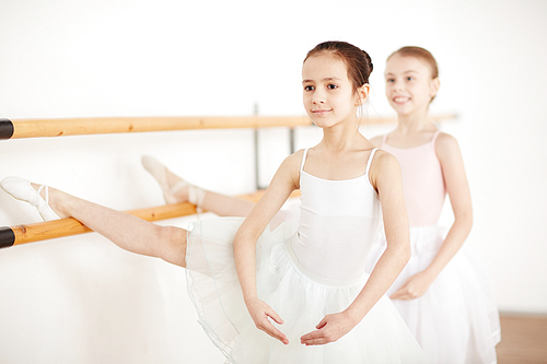 young girls in white clothes and pointe making stretching in dancing school side view