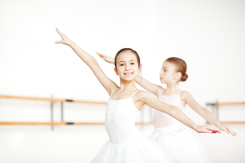 Two little girls outstretching arms while training in ballet class
