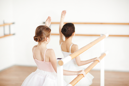 Unrecognizable little girls with beautiful hairstyle and classic clothes doing exercises at wooden machine