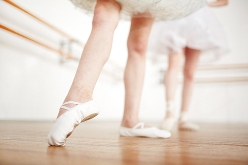 Faceless girls leg in ballet shoes making position on parquet with ballerina on background