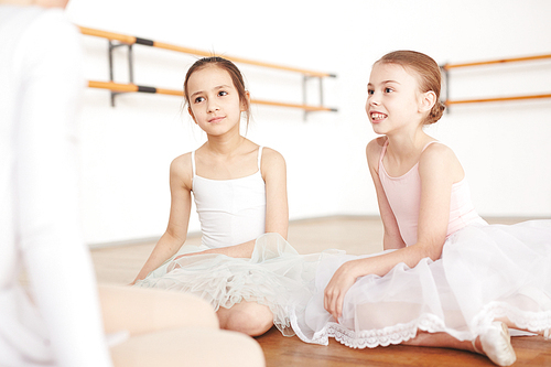 Focused girls in white tutu making attention on pedagogue in light dancing studio and smiling