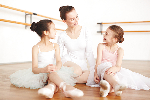 Adult ballerina sitting in light room with girls in white clothes and pointe in dancing studio