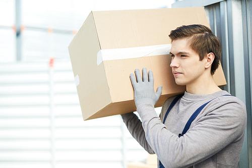 Young worker from relocation service carrying heavy carton package