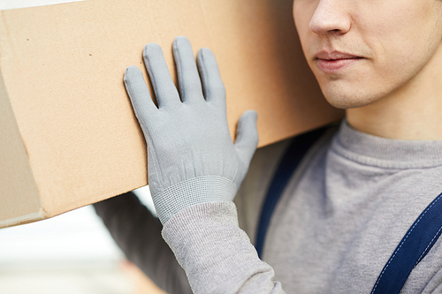 Close-up of content young mover in gloves carrying cardboard box on shoulder