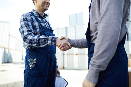 Two delivery men in workwear shaking hands of one another as symbol of agreement