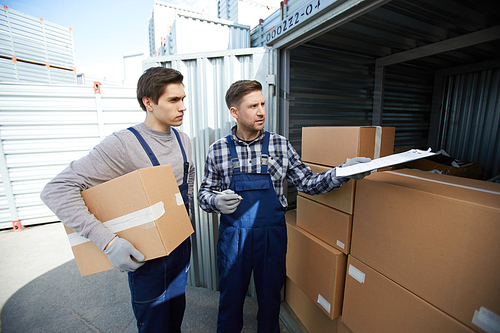 Young worker instructing his colleague about new cargo in large carton boxes