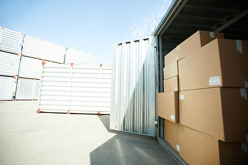 Open large metal container with stack of carboard boxes by day, container storage area