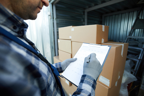 Close-up of busy cargo worker analyzing data in paper and marking information while taking goods