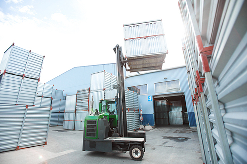 Modern powerful forklift truck lifting metal container while stacking it on others in outdoor storage area