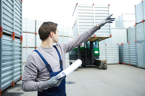 Young man in gloves and workwear showing where to put large storage container