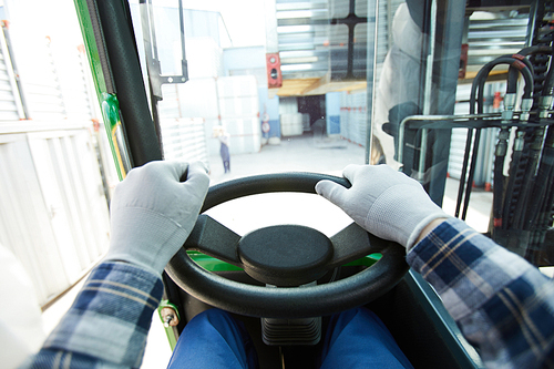 Close-up of unrecognizable truck driver in gloves holding steering wheel while driving truck over container storage area