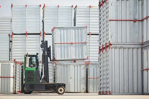 Stacks of new storage containers and load transportation machine on territory of modern organization