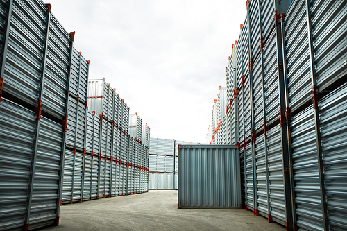Long corridor between stacks of new metallic storage containers on territory of load and transportation company