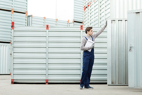 Serious handsome young man with clipboard holding cargo examination and opening modern metal shipment container at storage area