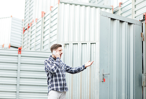 Young container owner in casual clothing using mobile phone while calling manager and gesturing when explaining his problem