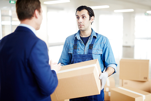 Gloved worker in uniform talking to businessman about where to remove boxes with office supplies