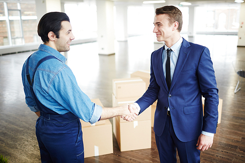 Young businessman in suit and delivery man in uniform handshaking after relocation work